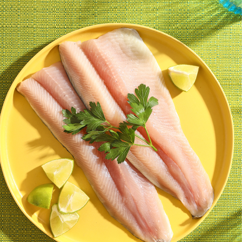 Two fresh fillets of Rainbow Trout plated on a yellow plate with lemon wedges.
