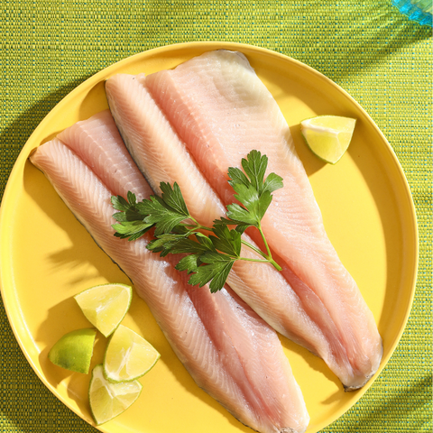 Two fresh fillets of Rainbow Trout plated on a yellow plate with lemon wedges.